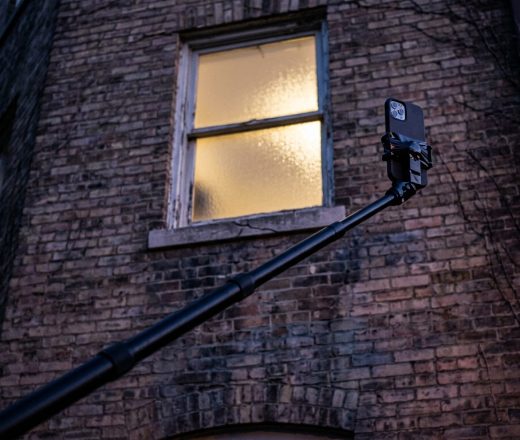 Un teléfono inteligente en un palo extensible apuntando hacia la ventana iluminada de un edificio de ladrillo