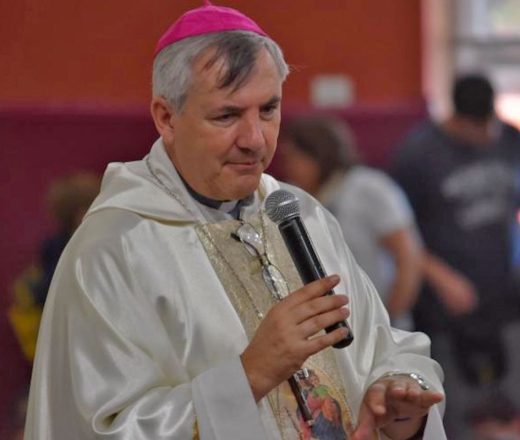 Obispo católico con vestiduras blancas y solideo rosa hablando por un micrófono