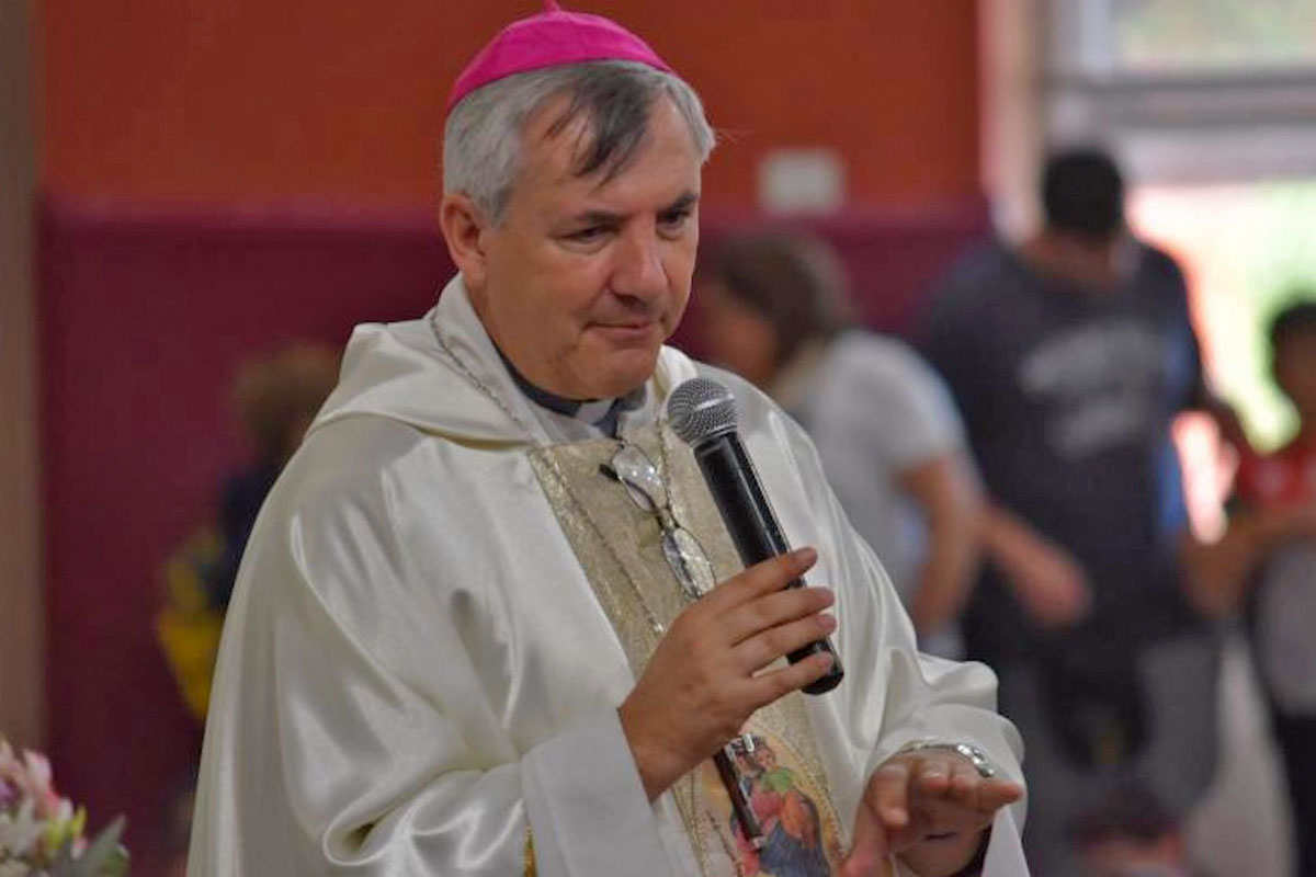 Obispo católico con vestiduras blancas y solideo rosa hablando por un micrófono